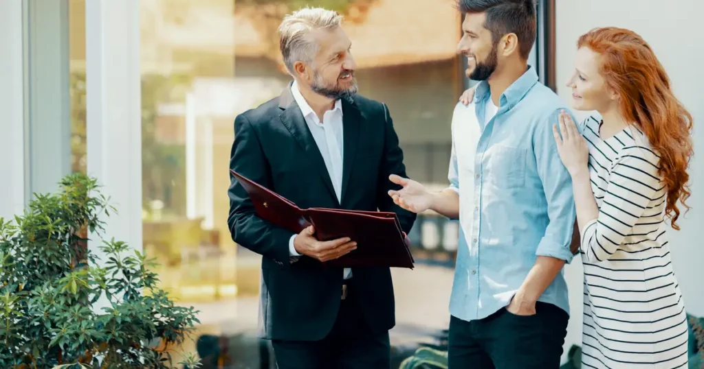 Real estate agent discussing home buying details with a smiling couple outside a modern house, holding a portfolio in hand.