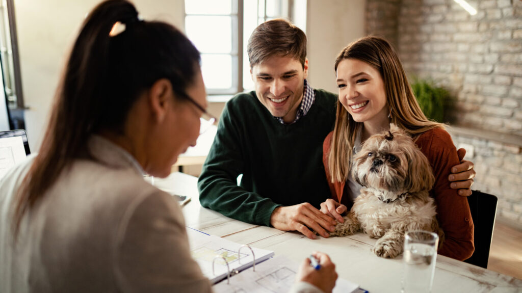 Young happy couple with a dog having a meeting with real estate agent in the office.