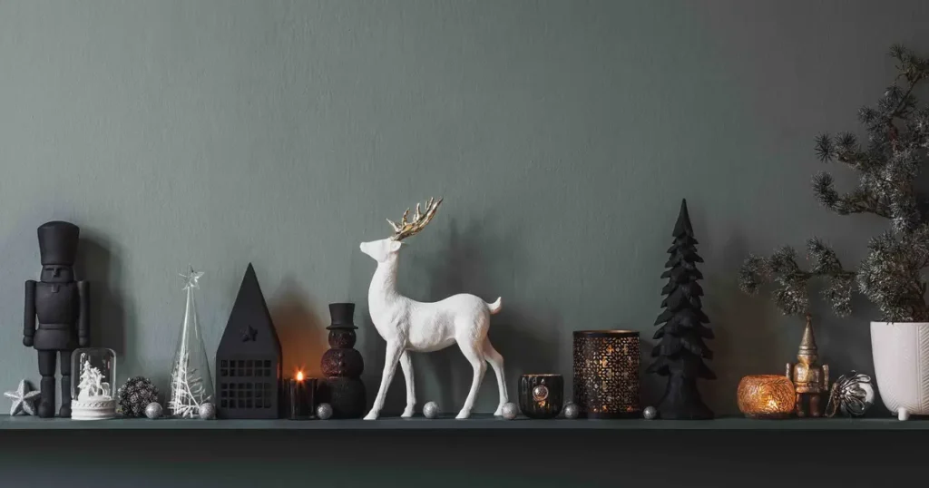 A stylish holiday mantel display with black, white, and gold decor, featuring a white reindeer figurine, candles, nutcrackers, and festive ornaments against a dark green wall.