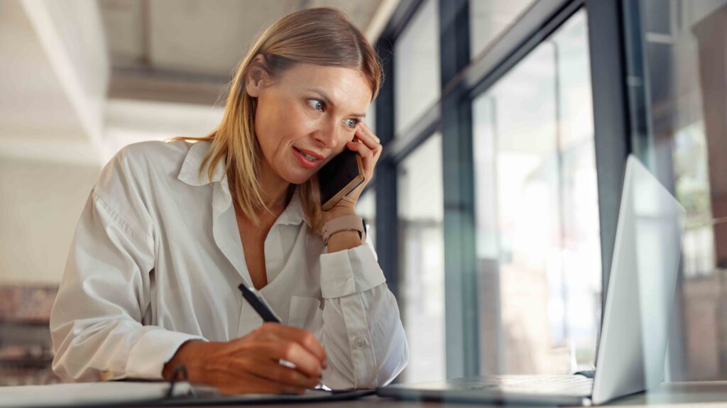 Woman manager talking by phone with client and use laptop while sitting in coworking