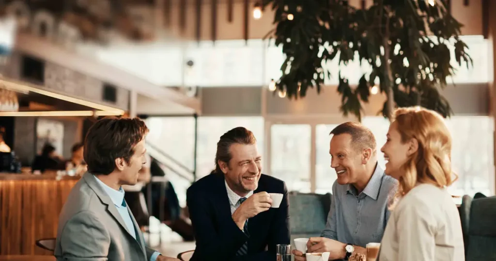 A group of professionals enjoying coffee and engaging in a lively conversation at a modern café, symbolizing networking and relationship building.