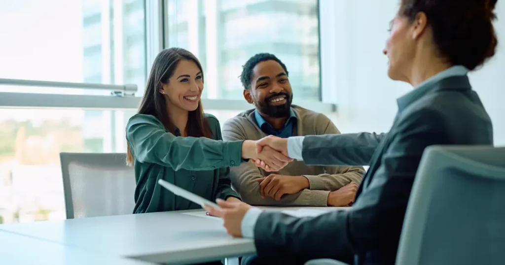 Smiling couple meeting with a professional advisor, shaking hands in a bright modern office setting.