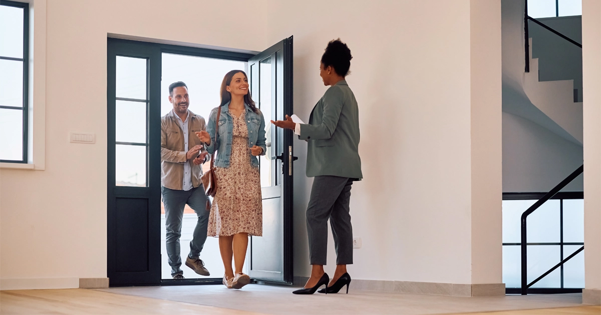 A real estate agent welcoming a smiling couple into a modern home for a showing, highlighting the home-buying experience.