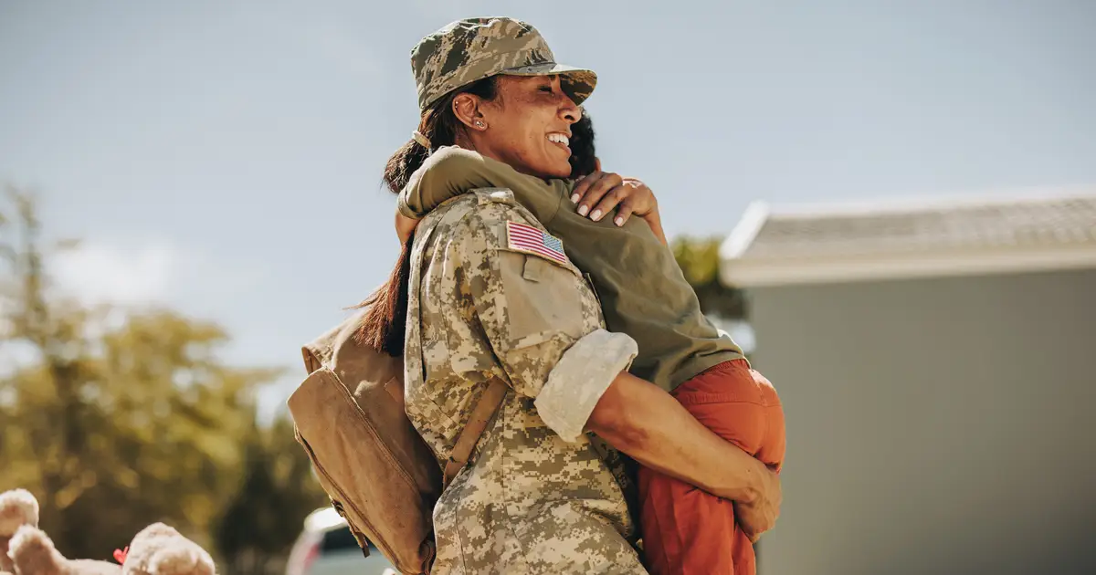 Uniformed servicemember hugging a child and smiling