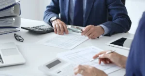 Hand holding magnifying glass over paperwork